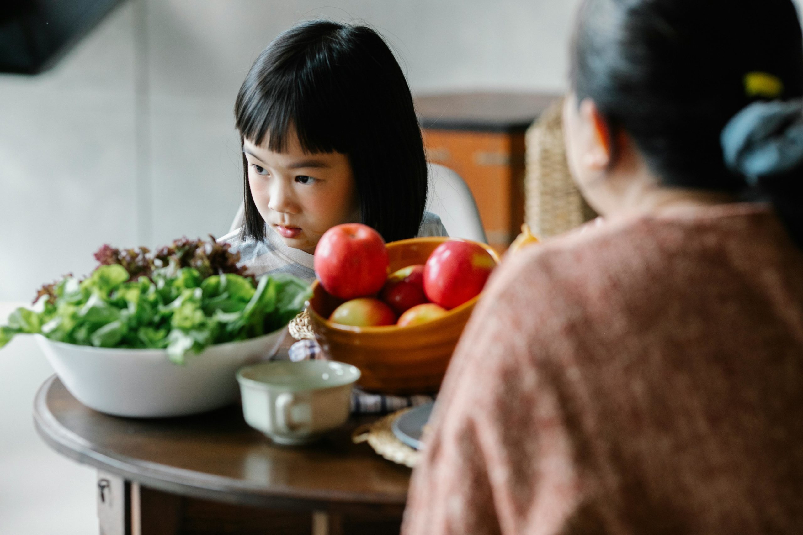 Ernstes Kleines Ethnisches Mädchen, Das Mit Mutter Während Des Mittagessens Am Tisch Sitzt Und Wegschaut