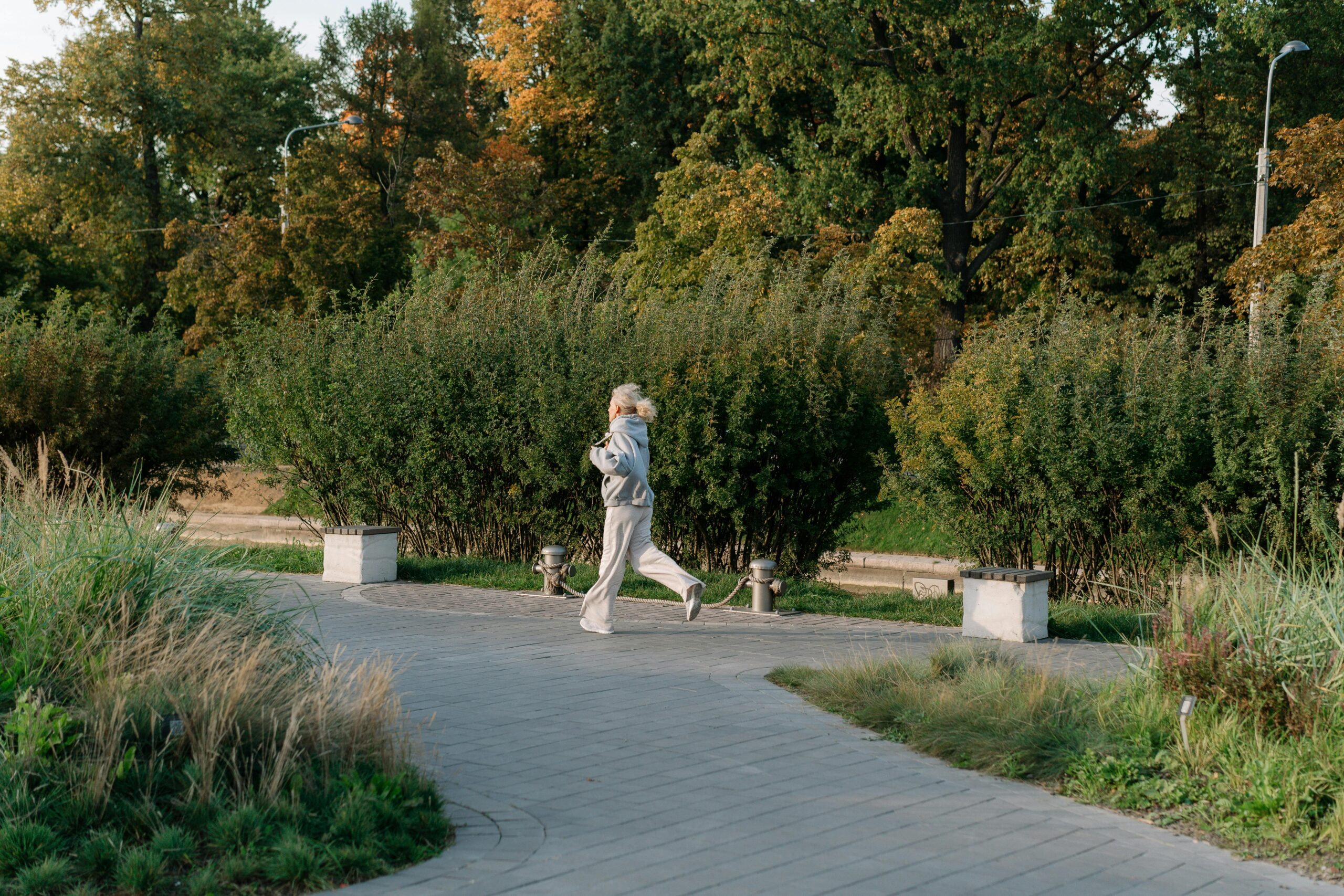 Eine Frau Im Grauen Hoodie, Die In Der Nähe Der Grünen Bäume Joggt